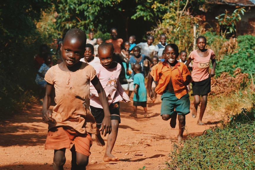 A group of African children run down a dirt path.