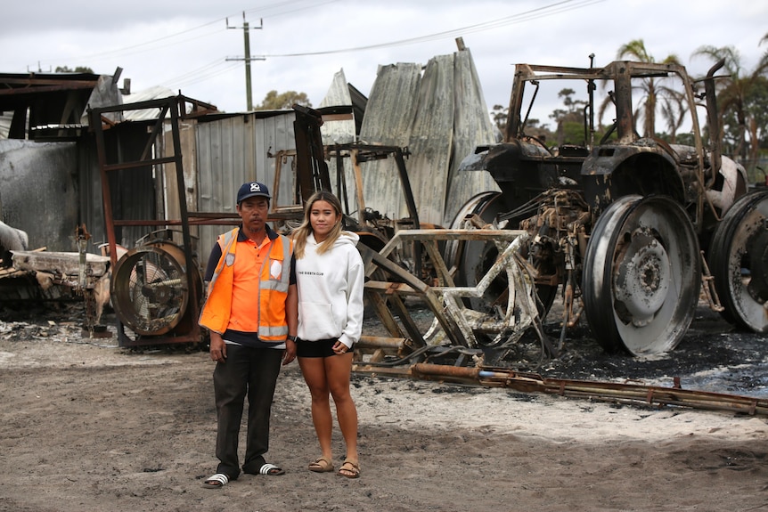 Tin Huynh and daughter Kathi stand in front of burnt-out machinery on the farm.