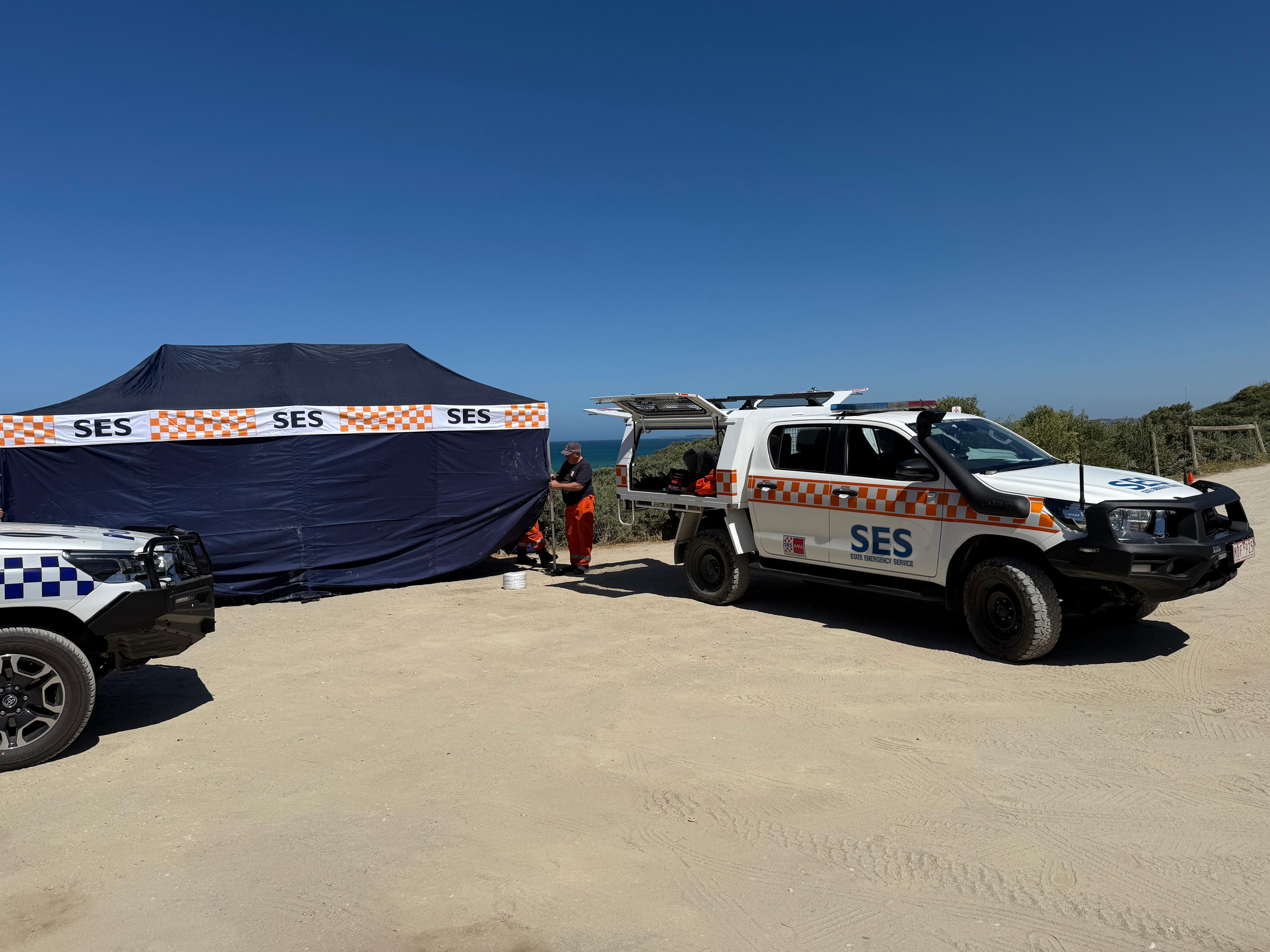 Uma foto de uma barraca azul marinho que diz "SSE"ao lado de um veículo da SES com céu azul ao fundo