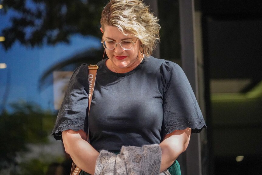 A woman walks away from a court house, looking serious and with her head bowed. 