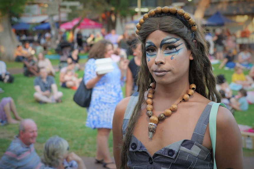 A drag artist stands in front of a crowd sitting on the grass