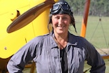 woman in pilot clothes standing in front of vintage plane