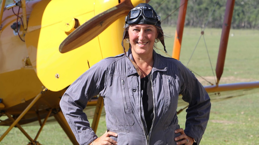 woman in pilot clothes standing in front of vintage plane