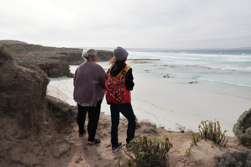 Back of two women looking out at sea over a clifftop.