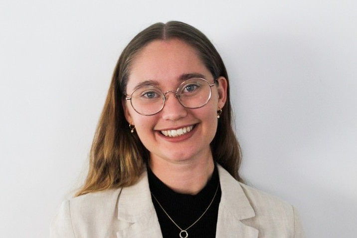Ashley Pade wearing glasses and a beige jacket, smiling in a portrait photo.