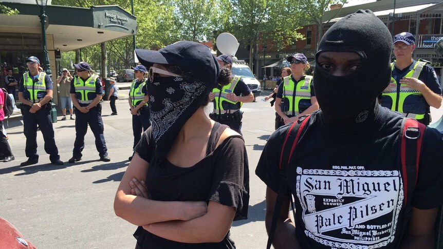 Activists in Bendigo cover their faces as police line up behind them.