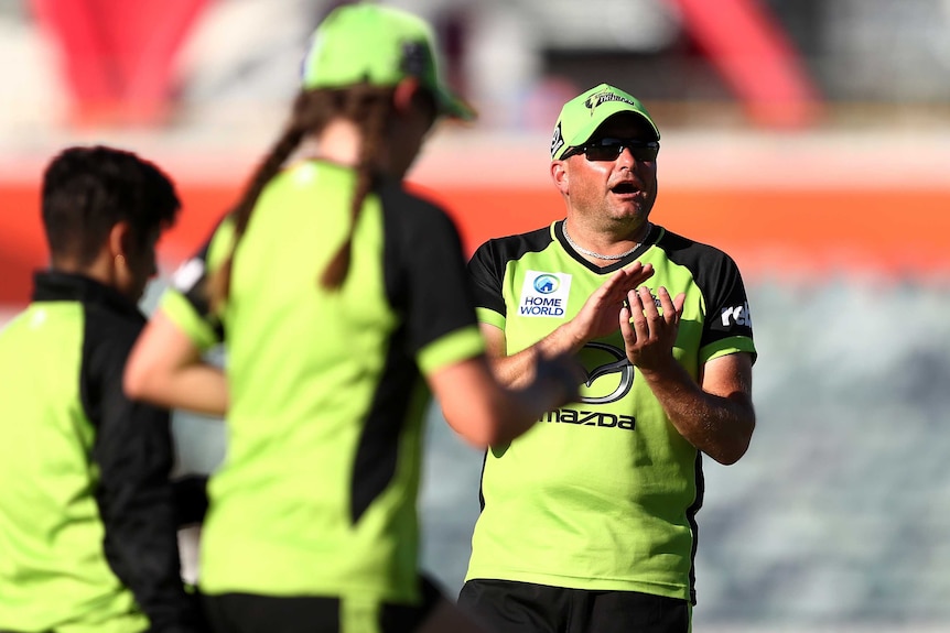 A cricket coach claps as his players get ready for a WBBL match.