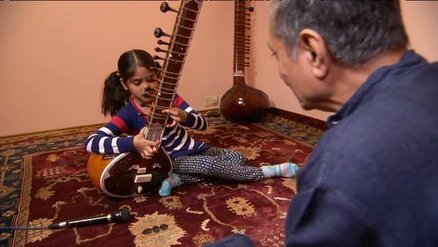 Indian girl plays sitar while elderly man sits nearby