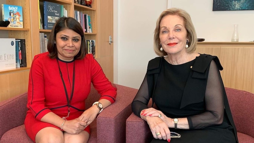 Two women dressed smartly sit on soft chairs facing and smiling at the camera - they are in Ita's office.