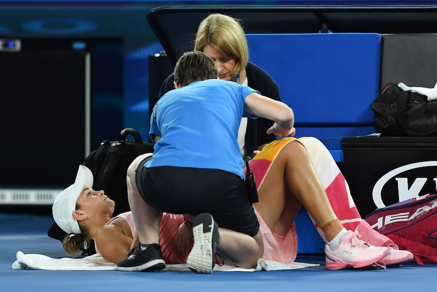 A female tennis player lies on the ground as two women kneel over her