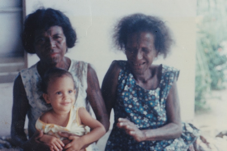 Two women baring traditional tattoos sit with a small child