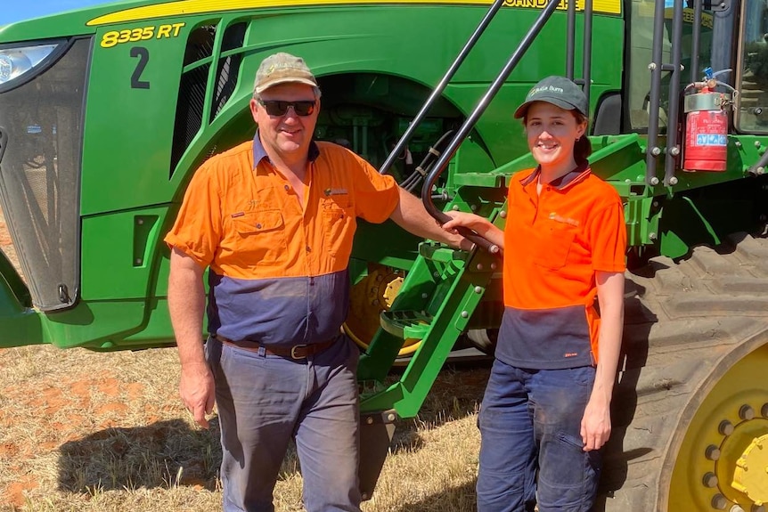 A man and a woman in orange hi vis stand in front of a green tractor