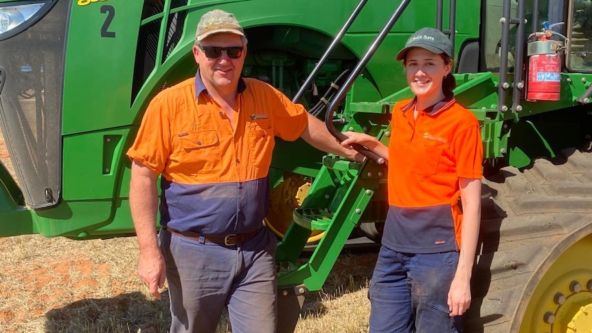 A man and a woman in orange hi vis stand in front of a green tractor