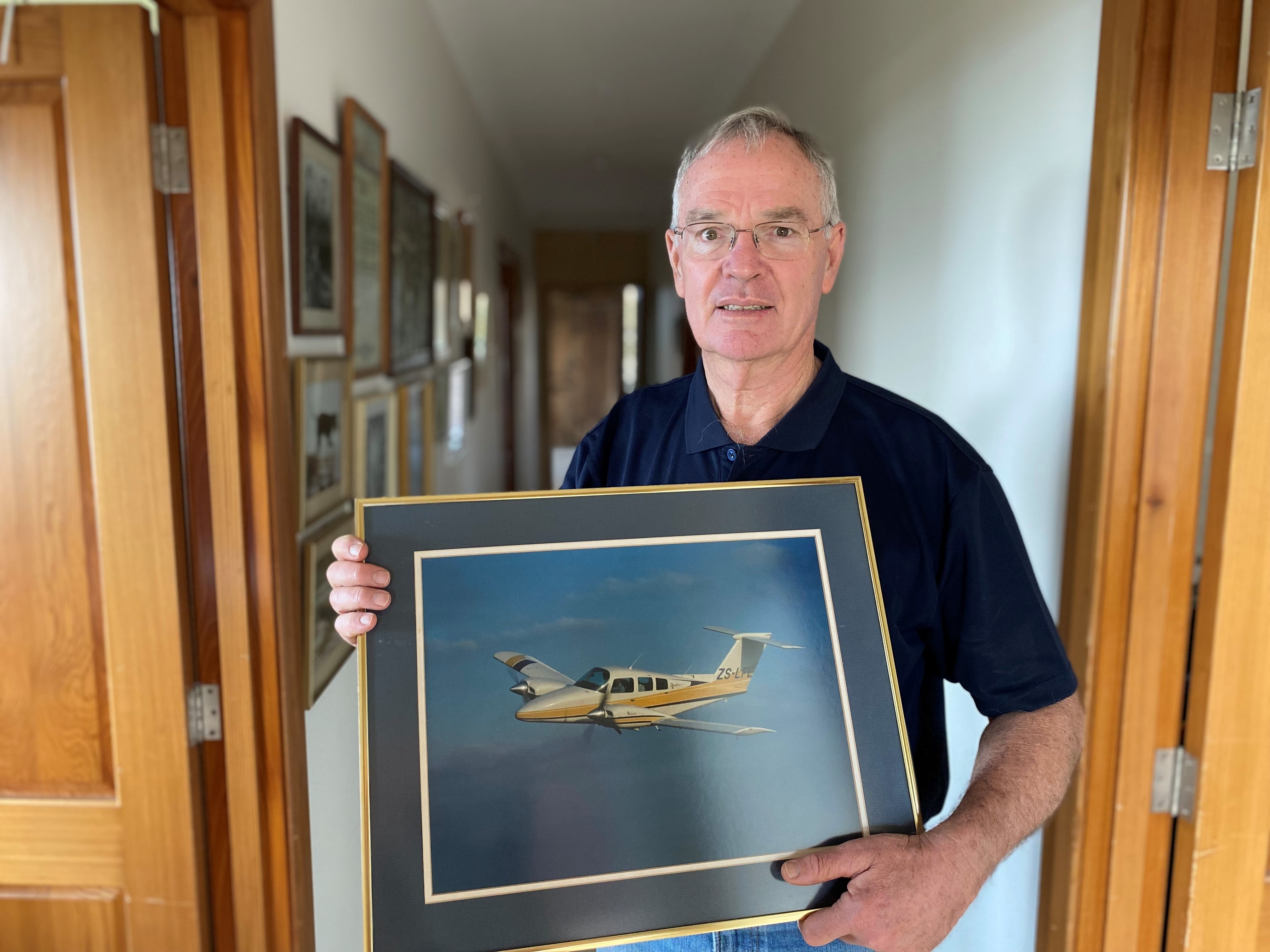 Man holding picture of an aeroplane in his hallway lined with other pictures