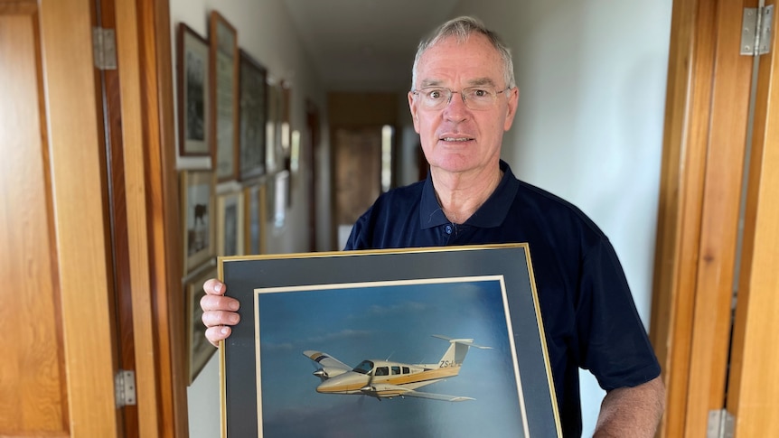 Man holding picture of an aeroplane in his hallway lined with other pictures