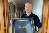 Man holding picture of an aeroplane in his hallway lined with other pictures