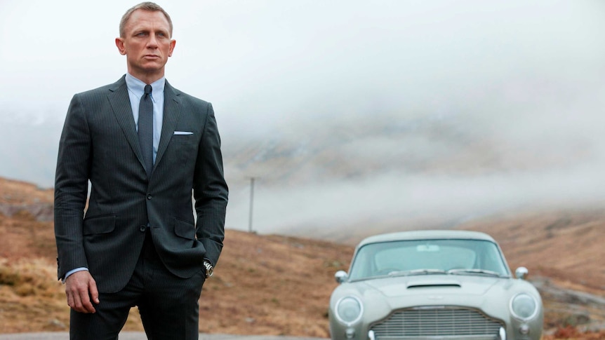 Daniel Craig, as James Bond, stands next to his Aston Martin in a scene from Skyfall.