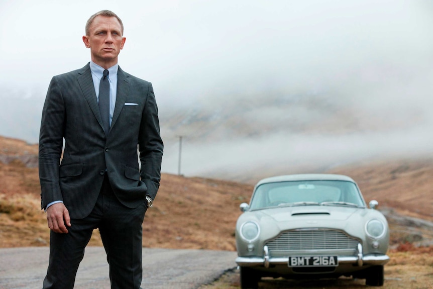 Daniel Craig, as James Bond, stands next to his Aston Martin in a scene from Skyfall.