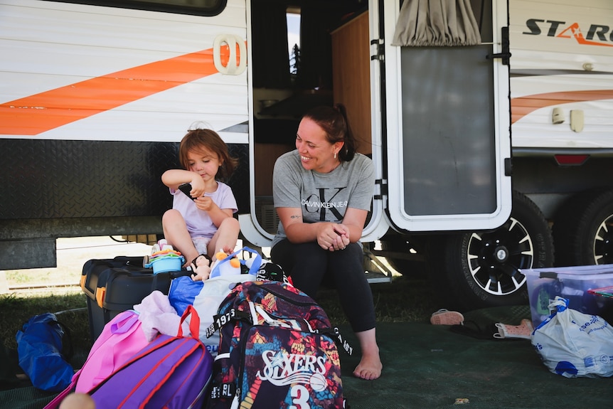 A woman watches a young girl play with toys on caravan step