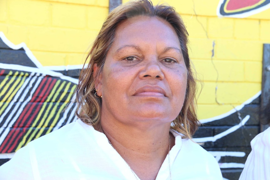 Helen Lee wears a white shirt and stands in front of a yellow wall