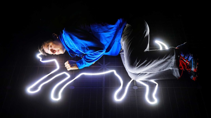 Actor Joshua Jenkins lies on his side over the lit-up outline of a dog.