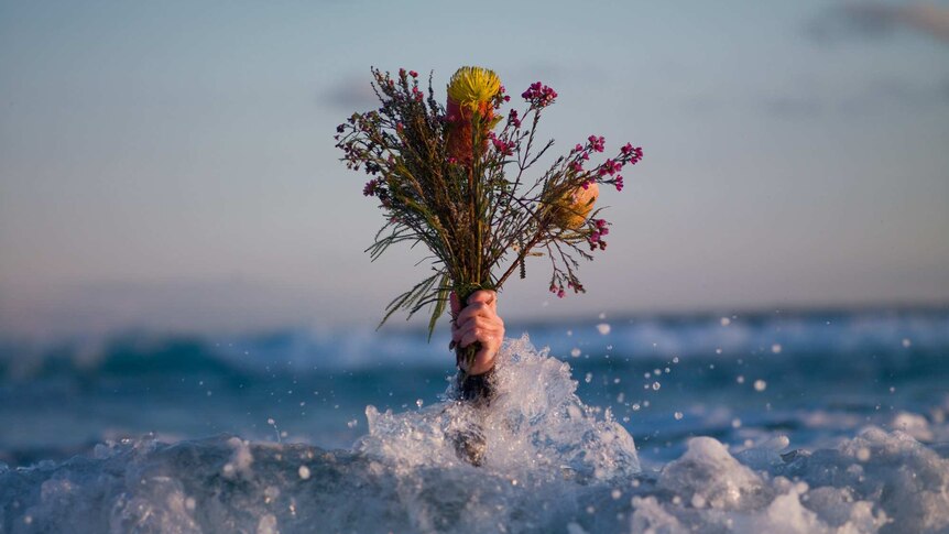 A hand holds a bunch of flowers in the ocean.