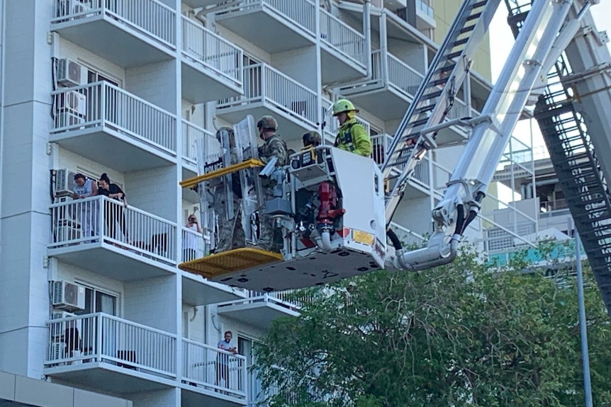 Police stand in a cherry picker in front of a white apartment building.