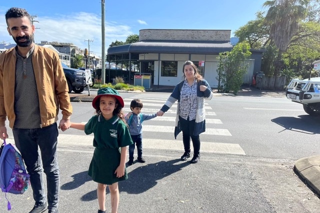 Syrian man and woman hold hands with a little boy and girl crossing the road. Their daughter is wearing a school uniform.