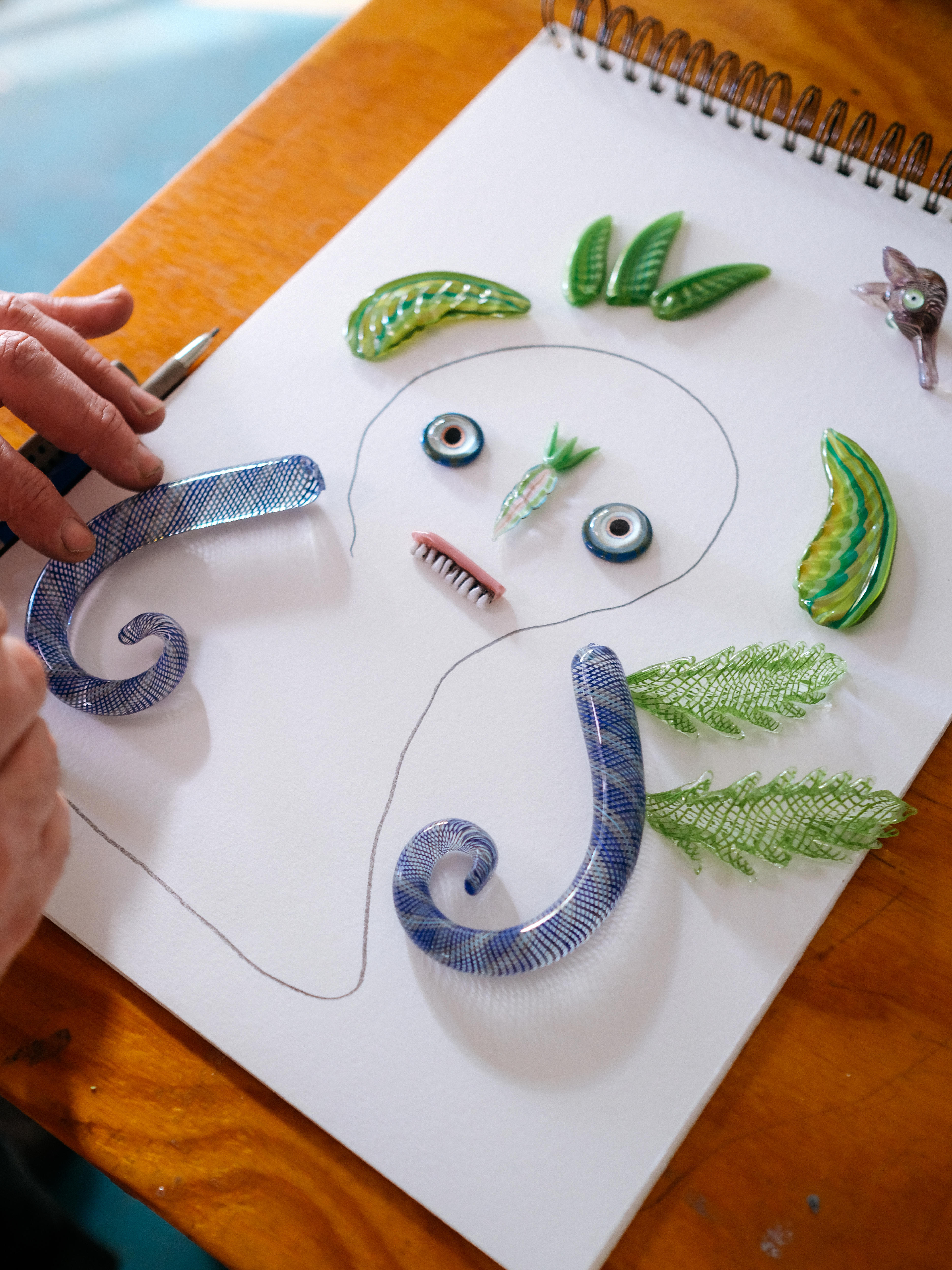 Close up on artist Tom Moore's hands arranging glass objects on a white paper, forming a funny character