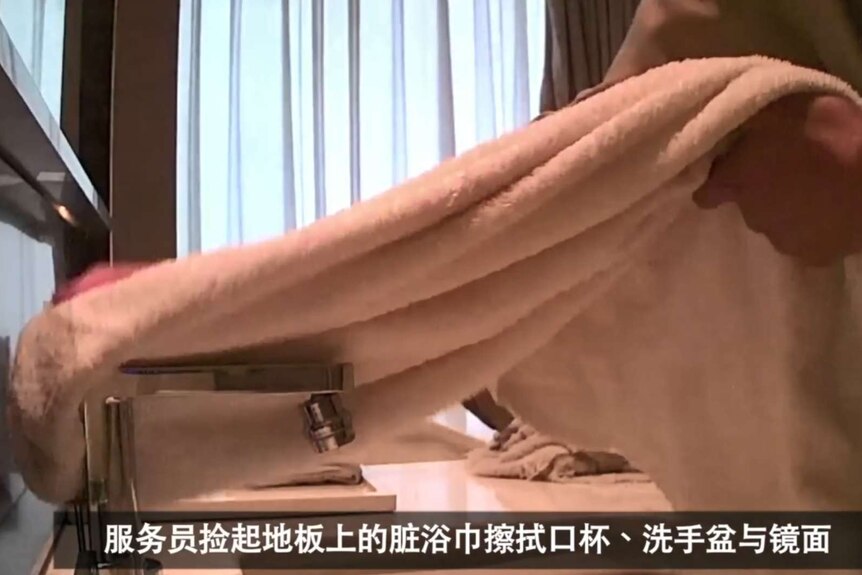 A hotel cleaner uses a used guest towel to wash a tap in a Chinese hotel room.