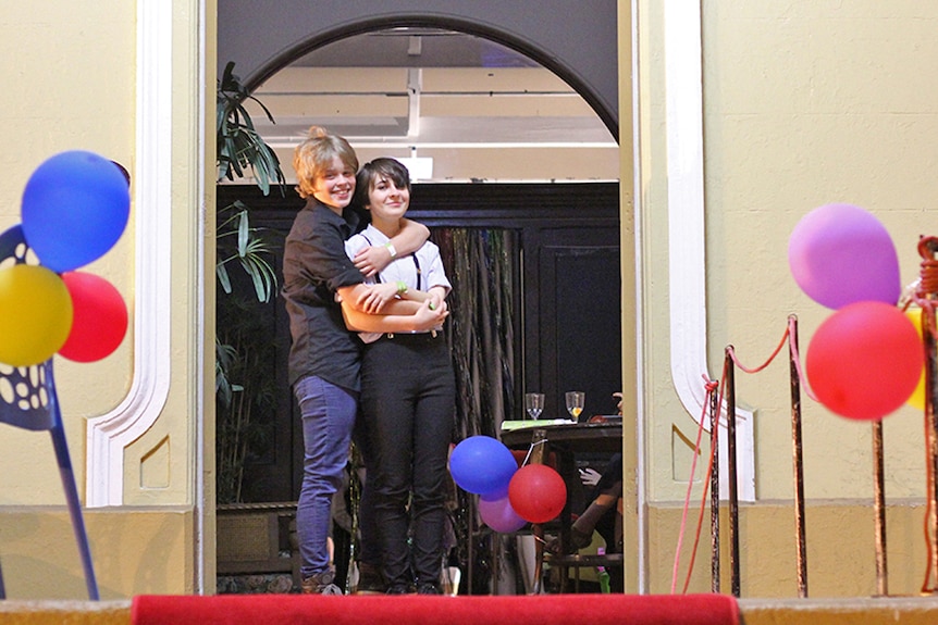 Two young women stand in the doorway of the Townsville Courthouse Theatre hugging.