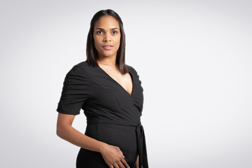 A woman in a black dress poses looking directly at the camera