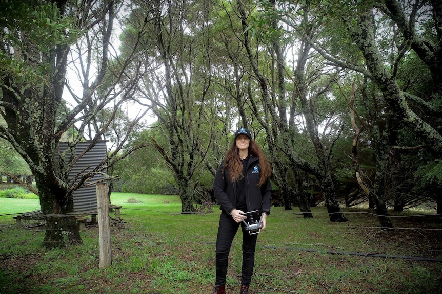 A woman standing surrounded by greenery with a camera.