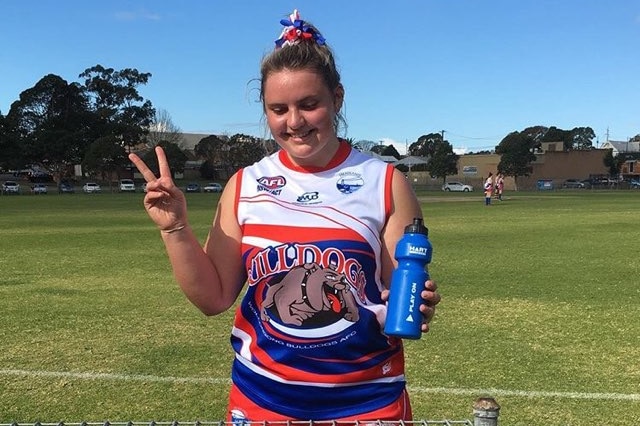 Gabby Frost gives a peace sign on a football oval dressed in her Aussie rules uniform.