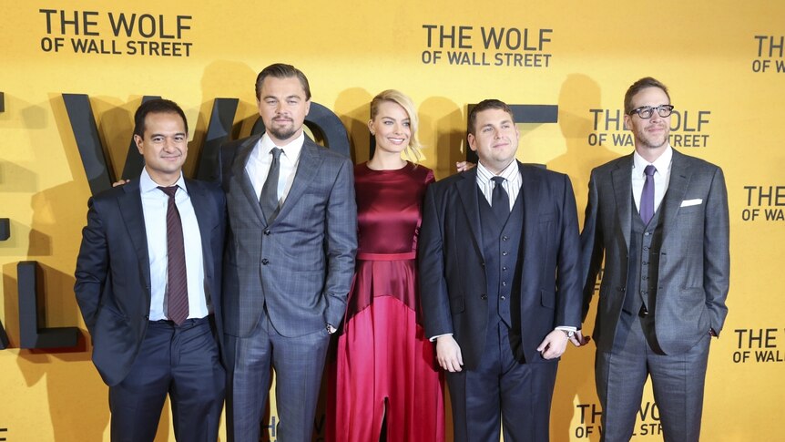 The two producers and three cast members stand on red carpet in front of yellow Wolf of Wall Street wall