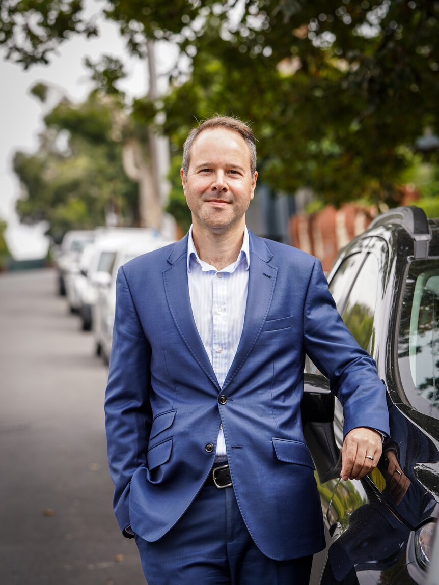 A portrait of a man in a suit, with cars in the background of a street