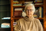 An elderly lady sits in front of a bookcase