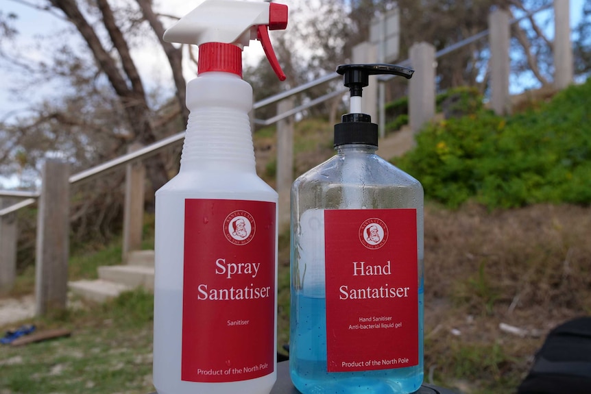Two spray bottles with the words 'spray santatiser' on the front, sitting on a container at the beach.