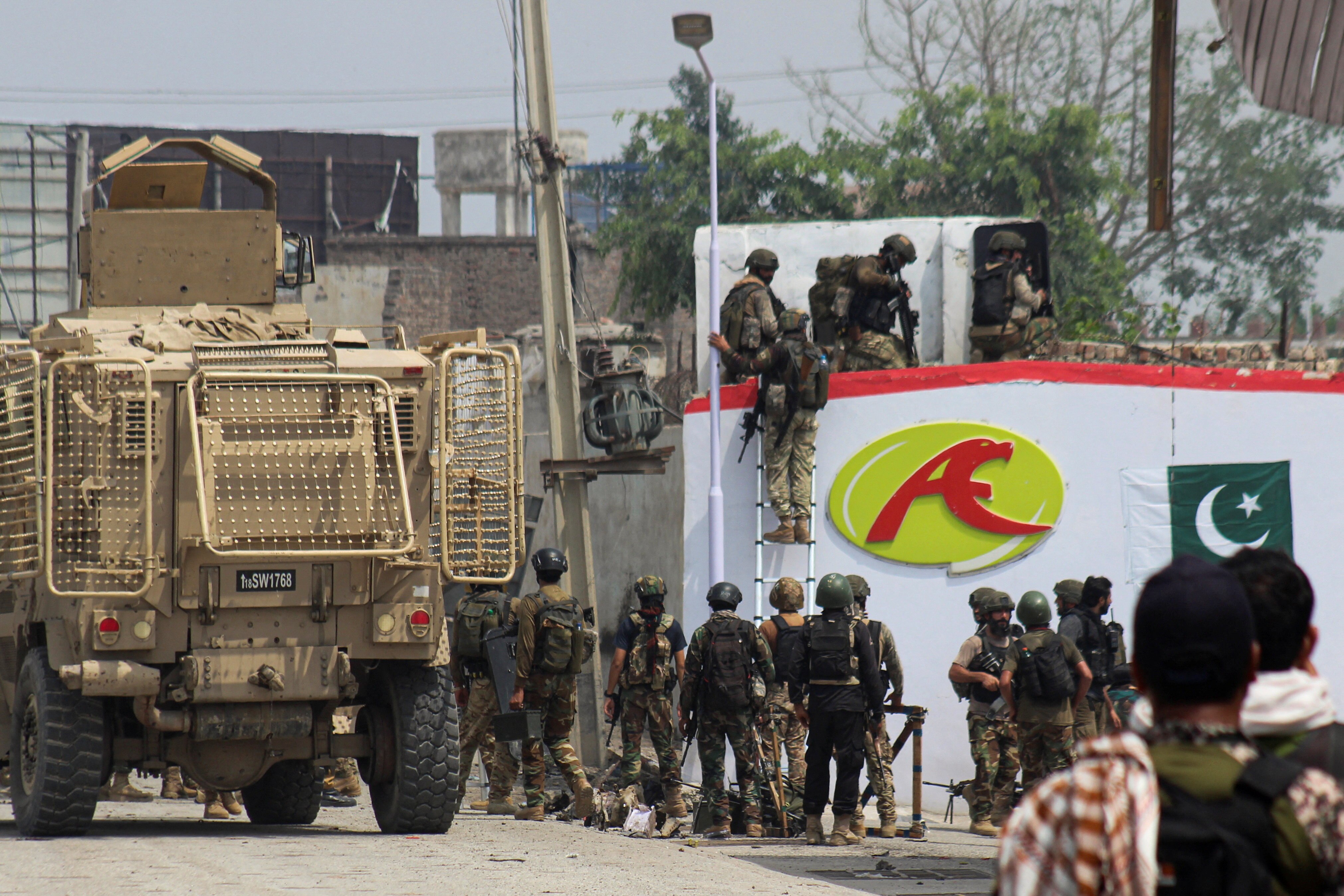 Pakistani military soldiers standing next to and atop a white building and an armoured truck