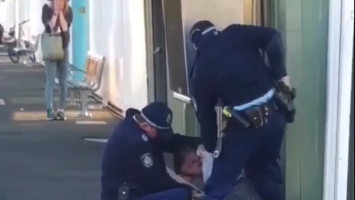 Officers arresting a man on a train platform as a woman looks on