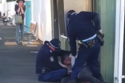 Officers arresting a man on a train platform as a woman looks on