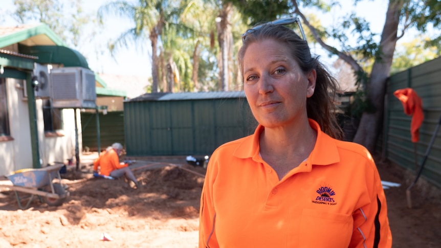 A woman in high vis stands in a dug up garden