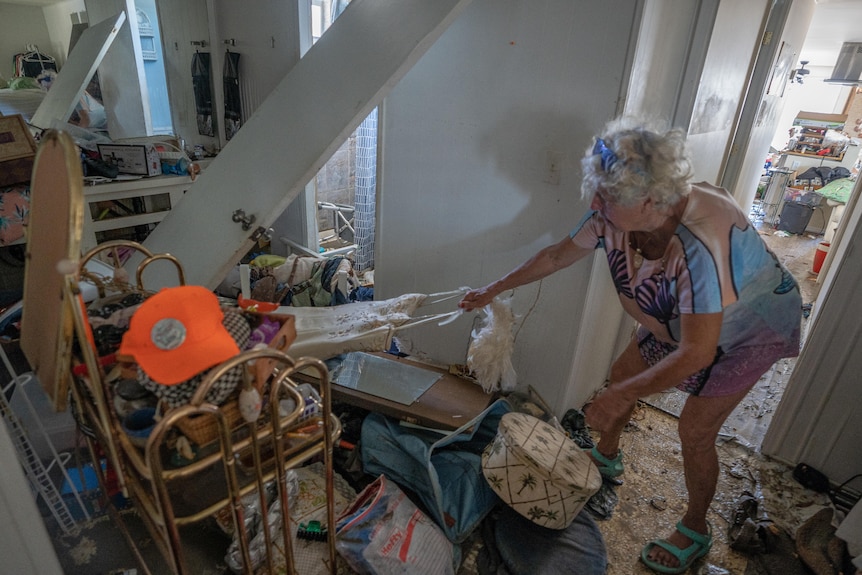 Woman pulling a costume out of rubble inside a house.