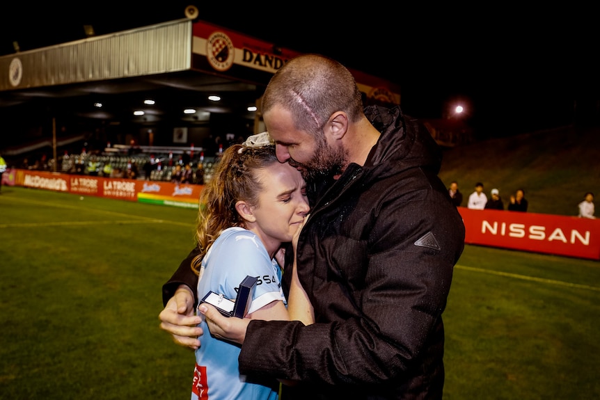 A tearful W-League player hugs her partner who is holding an engagement ring.