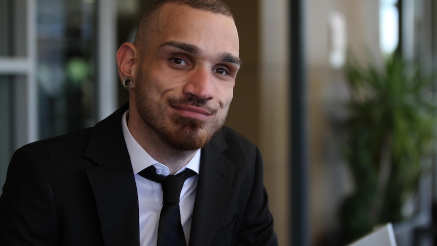 Uli Cartwright wearing a suit and tie, looking into the camera and smiling slightly.