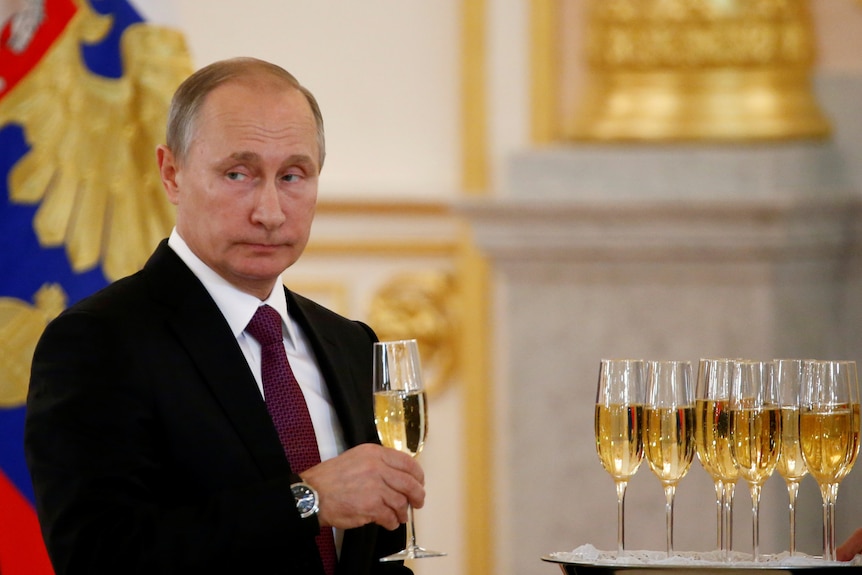 Vladimir Putin looking glum while holding a glass of champagne 