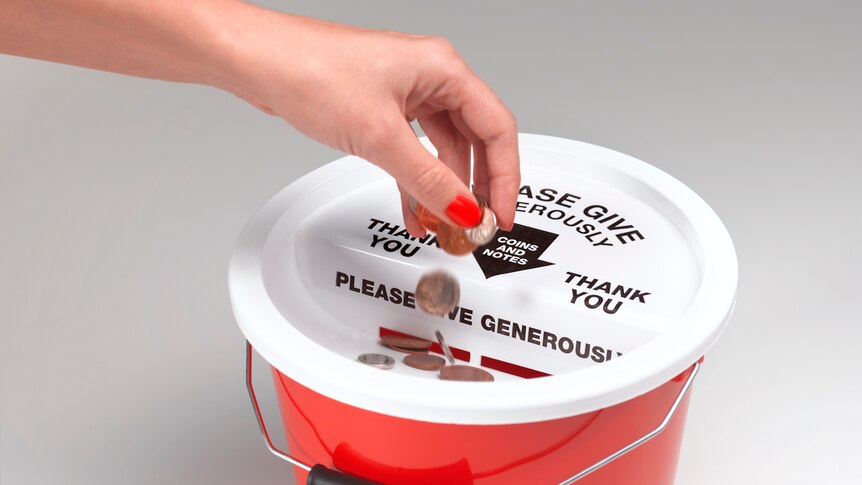 hand putting coins into ret bucket with white lid. Words on lid read 'please give generously, coins and notes, thank you'