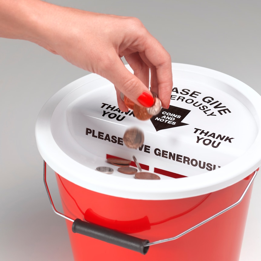 hand putting coins into ret bucket with white lid. Words on lid read 'please give generously, coins and notes, thank you'