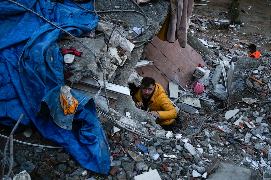 A man wearing bright yellow can be seen poking through the rubble. 