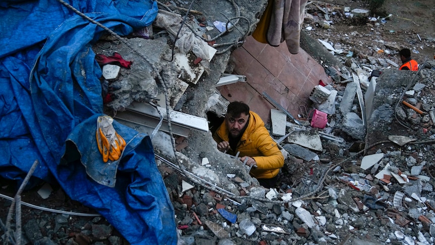 A man searches for people in a destroyed building.